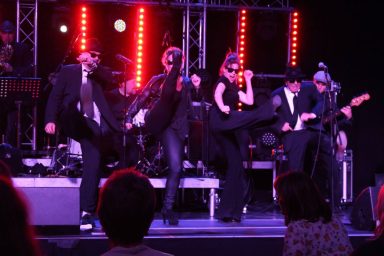 Fünf Musiker in Schwarz verführen mit Tanz und Gesang auf einer Bühne mit bunten Lichtern.