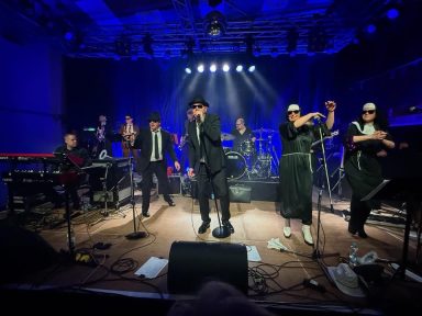 Ein musikalisches Ensemble auf der Bühne mit Live-Performern und Instrumenten.