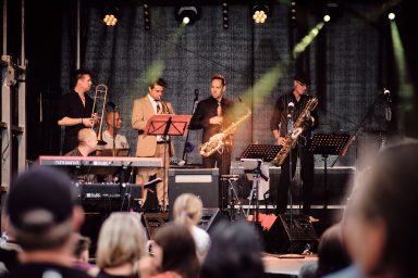 Eine Band spielt live auf einer Bühne, Zuschauer verfolgen die Aufführung.