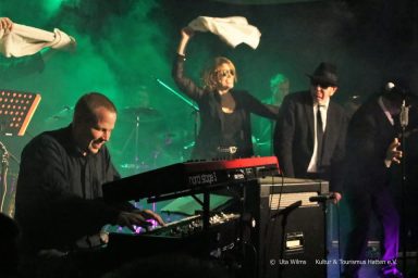 Musiker spielen auf einer Bühne, während eine Sängerin das Publikum anheizt.