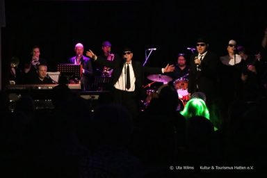 Liveband auf der Bühne mit performenden Musikern in stilvollen Outfits.