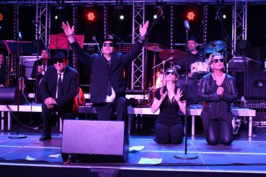 Vier Musiker auf der Bühne, in schwarz gekleidet, bei einer Performance.