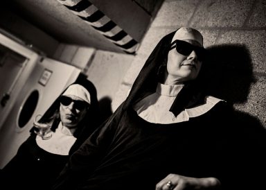Zwei Nonnen in traditioneller Kleidung und Sonnenbrillen in einem dunklen Raum.