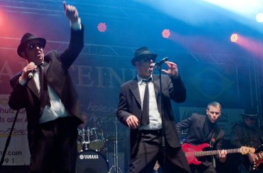 Zwei Sänger in Anzügen performen auf der Bühne, begleitet von einem Bassisten.