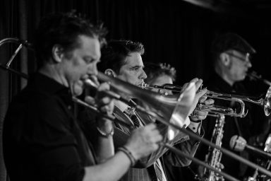 Vier Musiker spielen Posaune auf einer Bühne in Schwarz-Weiß.